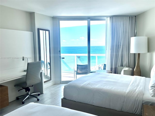 bedroom featuring floor to ceiling windows, access to outside, wood finished floors, and a water view