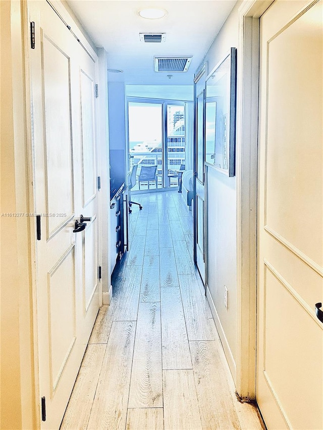 corridor featuring visible vents, baseboards, and light wood-style floors