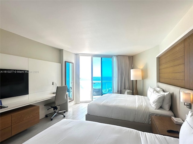 bedroom featuring a wall of windows, built in study area, access to exterior, and light wood finished floors