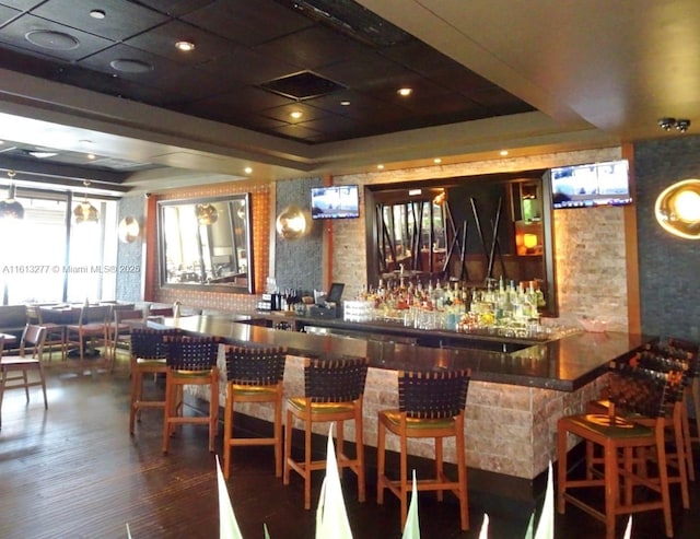 bar with a dry bar, a raised ceiling, and dark wood-type flooring