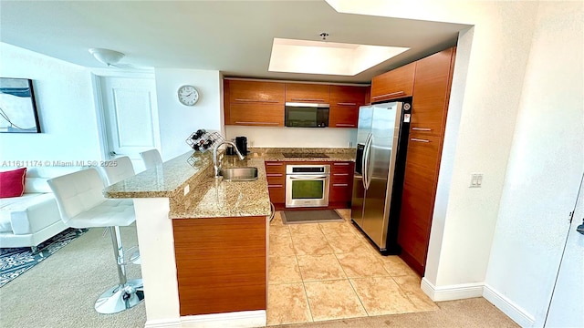 kitchen with kitchen peninsula, sink, appliances with stainless steel finishes, a breakfast bar area, and light stone counters