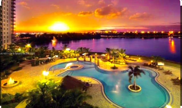 pool at dusk with a hot tub, a water view, and a patio