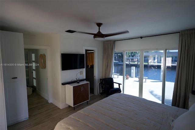 bedroom featuring access to outside, hardwood / wood-style flooring, ceiling fan, and a water view