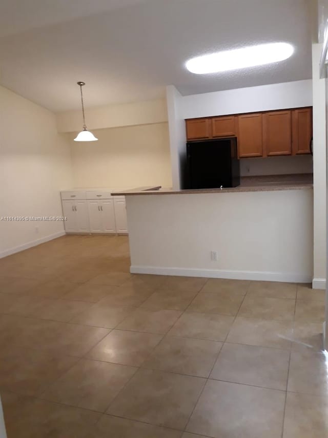 kitchen with light tile patterned floors, kitchen peninsula, fridge, and decorative light fixtures