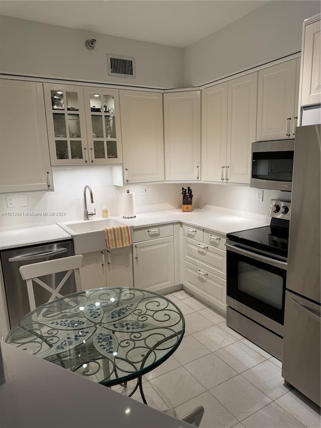 kitchen featuring visible vents, a sink, stainless steel appliances, light countertops, and glass insert cabinets