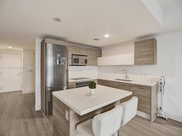 kitchen with sink, light hardwood / wood-style flooring, appliances with stainless steel finishes, and a center island