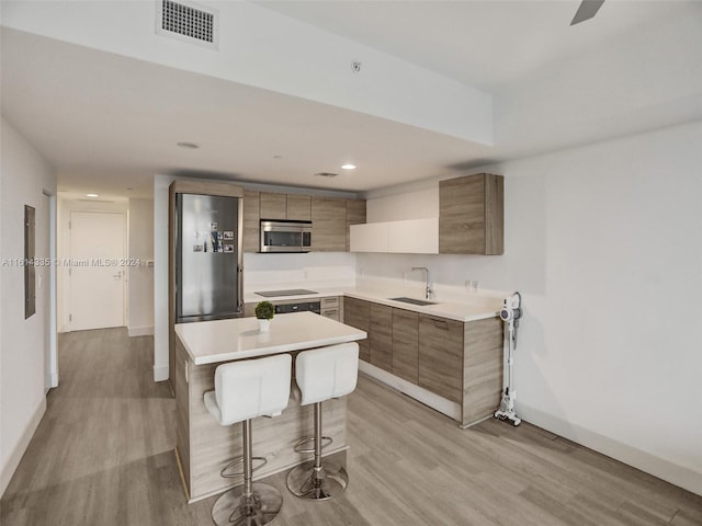 kitchen with sink, appliances with stainless steel finishes, a kitchen bar, light hardwood / wood-style flooring, and a kitchen island