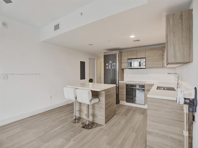 kitchen featuring black appliances, light wood-type flooring, a kitchen bar, sink, and a center island