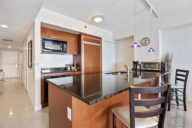 kitchen with dark stone counters, sink, an island with sink, decorative light fixtures, and a kitchen bar