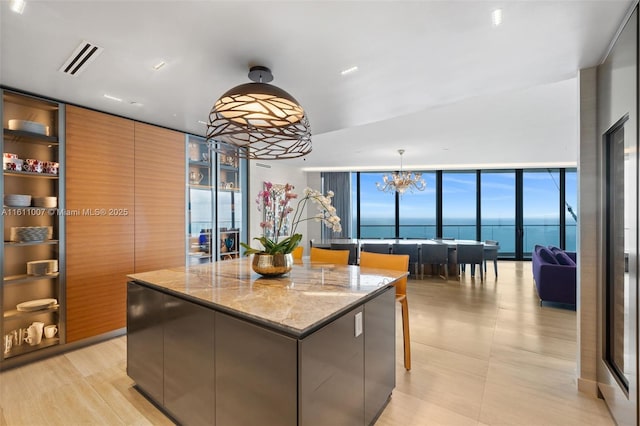 kitchen featuring a water view, an inviting chandelier, decorative light fixtures, a center island, and light stone countertops