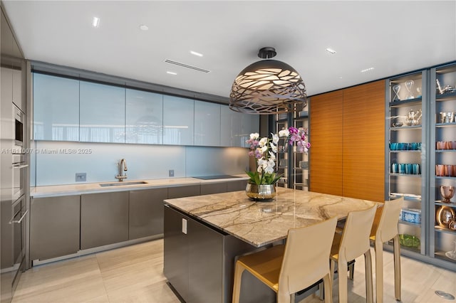 kitchen featuring sink, a breakfast bar area, hanging light fixtures, a center island, and light stone counters