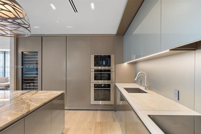 kitchen with sink, gray cabinetry, light stone countertops, stainless steel double oven, and black electric cooktop