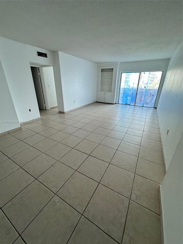 spare room with light tile patterned floors, built in features, and a textured ceiling