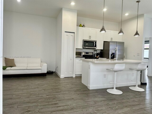 kitchen featuring white cabinets, decorative light fixtures, stainless steel appliances, dark hardwood / wood-style floors, and a kitchen island with sink