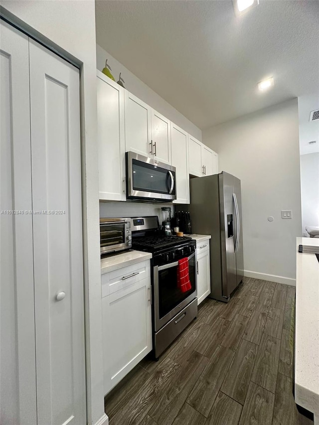 kitchen with dark wood-type flooring, a textured ceiling, stainless steel appliances, and white cabinets