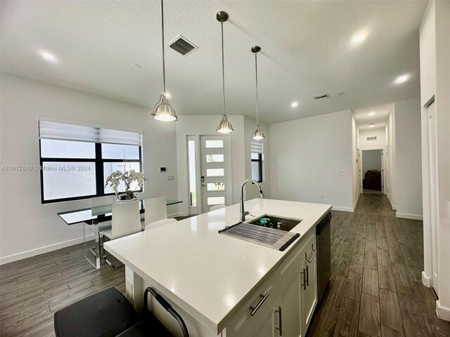 kitchen with sink, dark wood-type flooring, pendant lighting, a center island with sink, and a textured ceiling