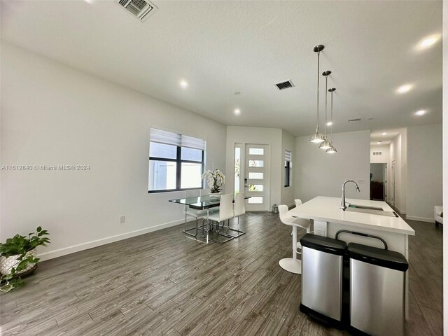 kitchen with a textured ceiling, dark hardwood / wood-style flooring, pendant lighting, an island with sink, and sink