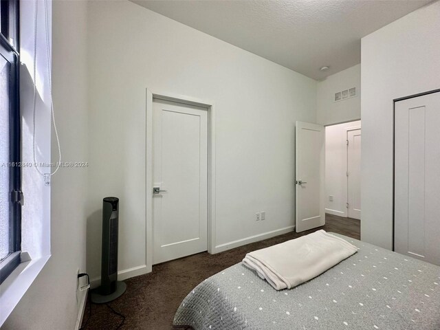 bedroom featuring multiple windows, a textured ceiling, and dark colored carpet