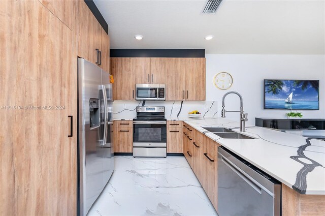 kitchen with light tile patterned floors, appliances with stainless steel finishes, sink, light stone counters, and kitchen peninsula