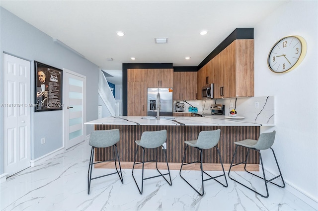 kitchen featuring kitchen peninsula, appliances with stainless steel finishes, light tile patterned floors, backsplash, and a breakfast bar area