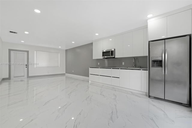 kitchen featuring stainless steel appliances, sink, light tile patterned floors, decorative backsplash, and white cabinetry