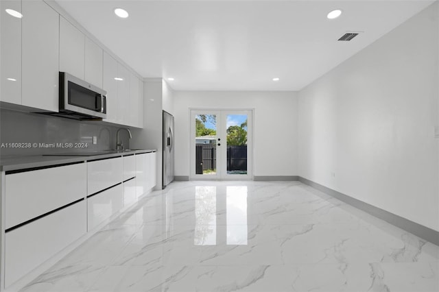 kitchen featuring light tile patterned flooring, white cabinetry, french doors, appliances with stainless steel finishes, and sink