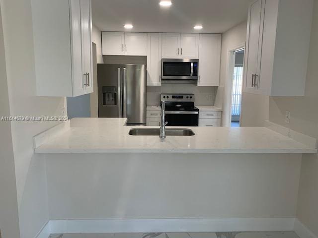 kitchen with appliances with stainless steel finishes, white cabinetry, light stone countertops, and sink