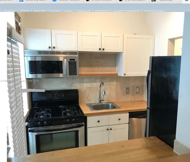 kitchen with wood counters, backsplash, white cabinetry, appliances with stainless steel finishes, and sink