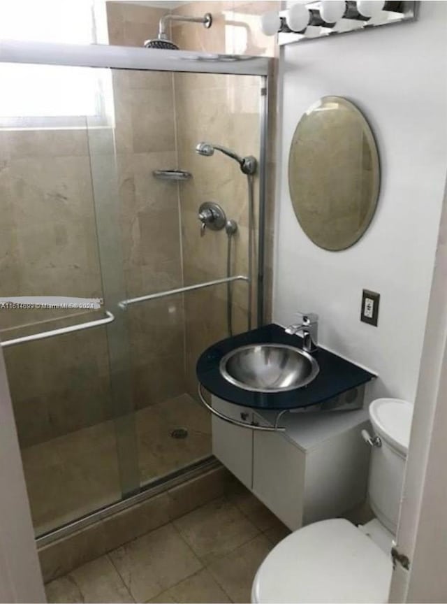 bathroom featuring a shower with door, tile flooring, toilet, and vanity