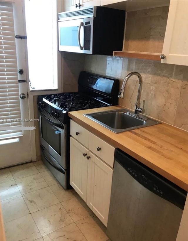 kitchen featuring tasteful backsplash, stainless steel appliances, wooden counters, sink, and white cabinetry