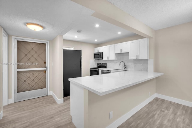 kitchen featuring white cabinetry, kitchen peninsula, stainless steel appliances, a textured ceiling, and light hardwood / wood-style flooring