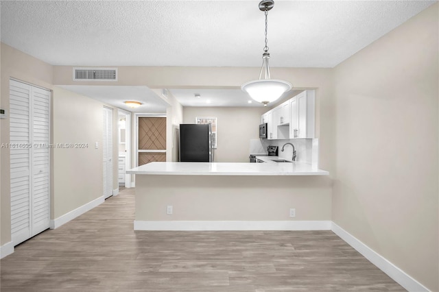 kitchen featuring pendant lighting, kitchen peninsula, white cabinets, and black refrigerator