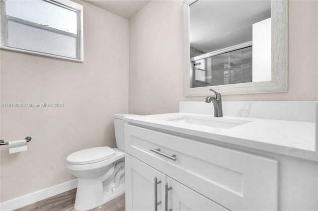 bathroom featuring wood-type flooring, vanity, a shower with shower door, and toilet