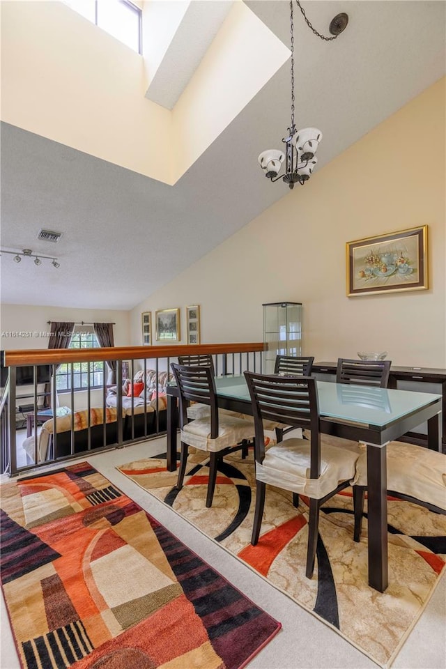 carpeted dining space with high vaulted ceiling, a chandelier, and track lighting