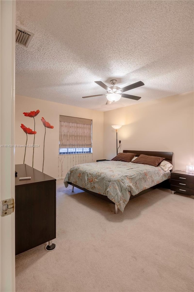 bedroom with ceiling fan, light colored carpet, and a textured ceiling