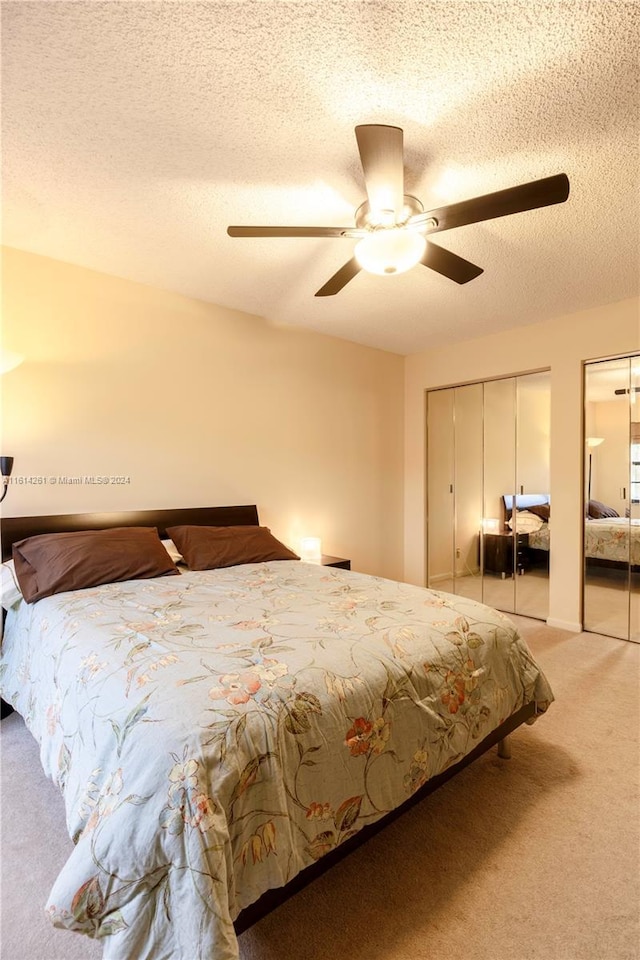 bedroom with multiple closets, ceiling fan, light colored carpet, and a textured ceiling