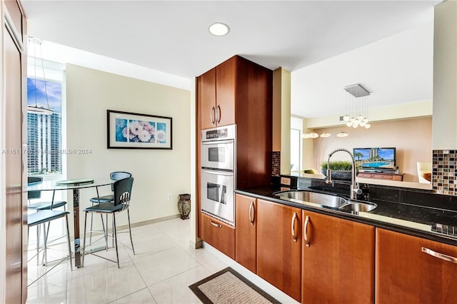 kitchen with backsplash, double oven, sink, pendant lighting, and dark stone countertops