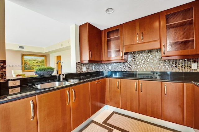 kitchen with black electric stovetop, backsplash, dark stone countertops, and sink