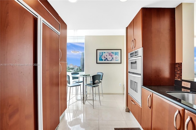 kitchen with decorative backsplash, double oven, sink, light tile patterned floors, and dark stone countertops