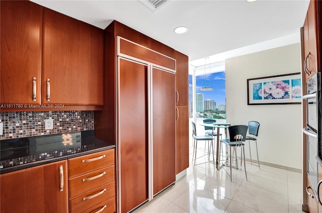 kitchen with paneled refrigerator, light tile patterned floors, dark stone countertops, tasteful backsplash, and wall oven