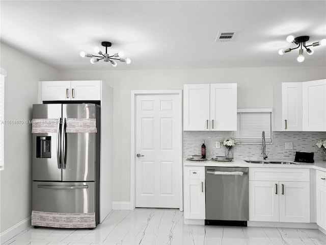 kitchen with white cabinets, sink, backsplash, appliances with stainless steel finishes, and a notable chandelier