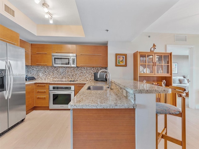 kitchen with a breakfast bar, kitchen peninsula, sink, appliances with stainless steel finishes, and light stone counters