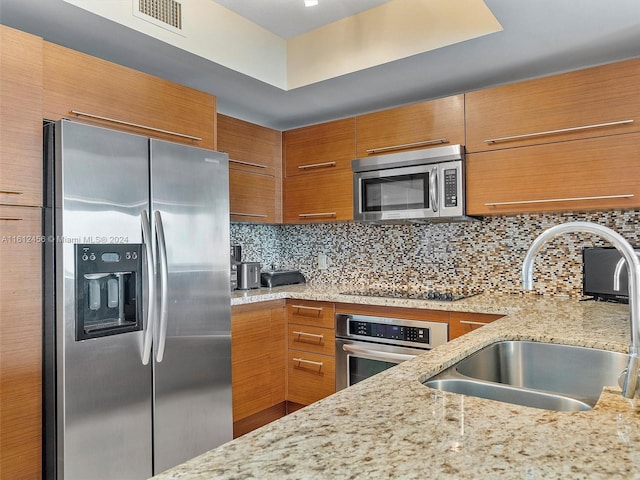 kitchen featuring decorative backsplash, appliances with stainless steel finishes, sink, and light stone counters