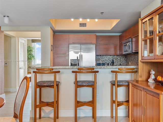 kitchen featuring stainless steel appliances, a kitchen bar, backsplash, and light stone counters