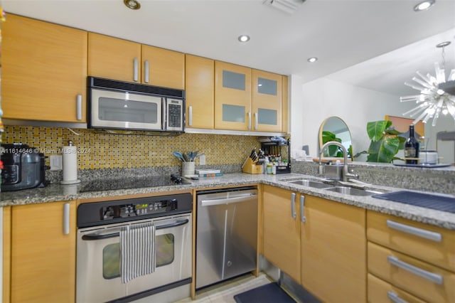 kitchen with appliances with stainless steel finishes, an inviting chandelier, sink, and light stone counters