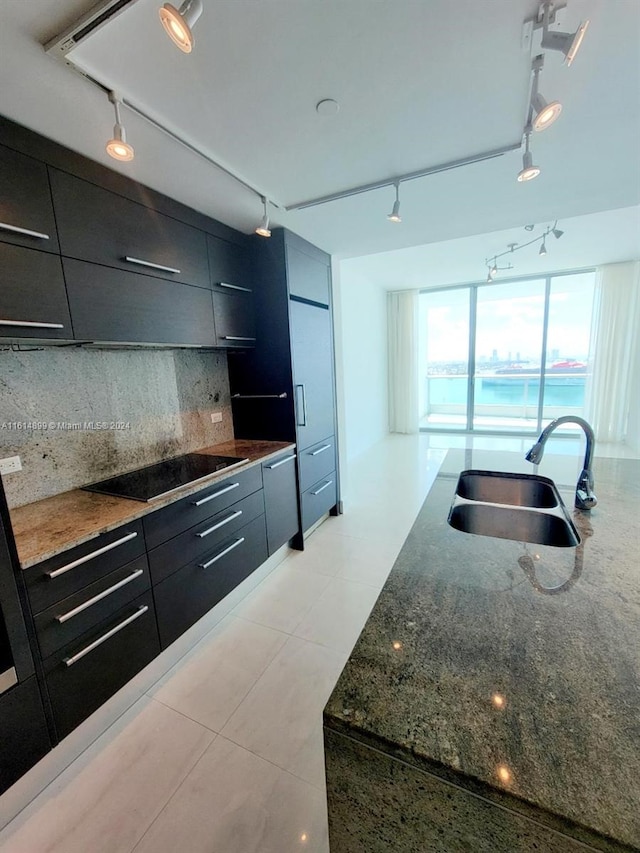 kitchen with sink, rail lighting, backsplash, dark stone counters, and black electric cooktop