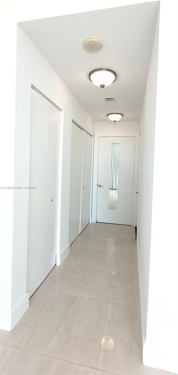 hall featuring baseboards, visible vents, and light tile patterned floors