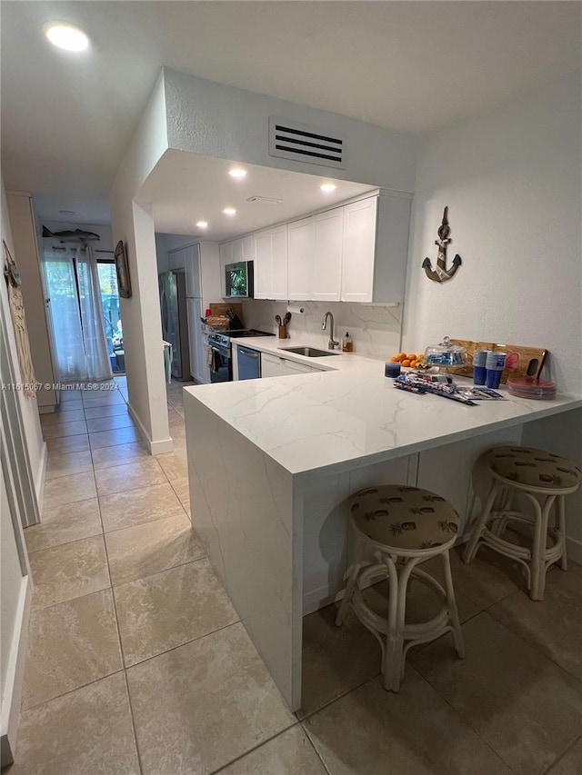 kitchen with kitchen peninsula, light stone counters, sink, white cabinetry, and a breakfast bar area