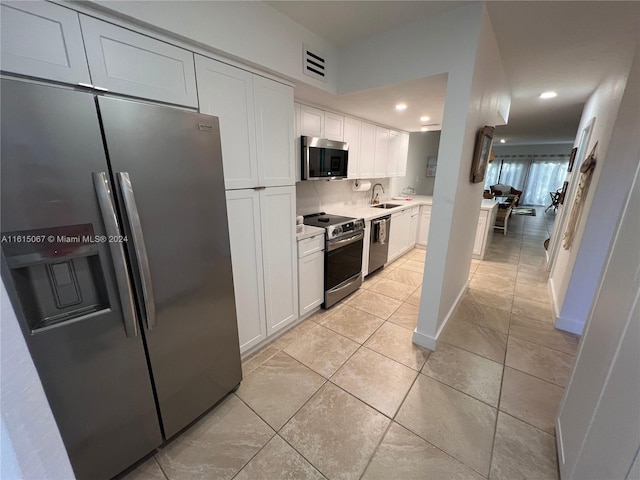 kitchen with sink, stainless steel appliances, light tile patterned floors, kitchen peninsula, and white cabinets