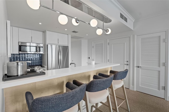 kitchen featuring hanging light fixtures, white cabinetry, stainless steel appliances, ornamental molding, and light colored carpet